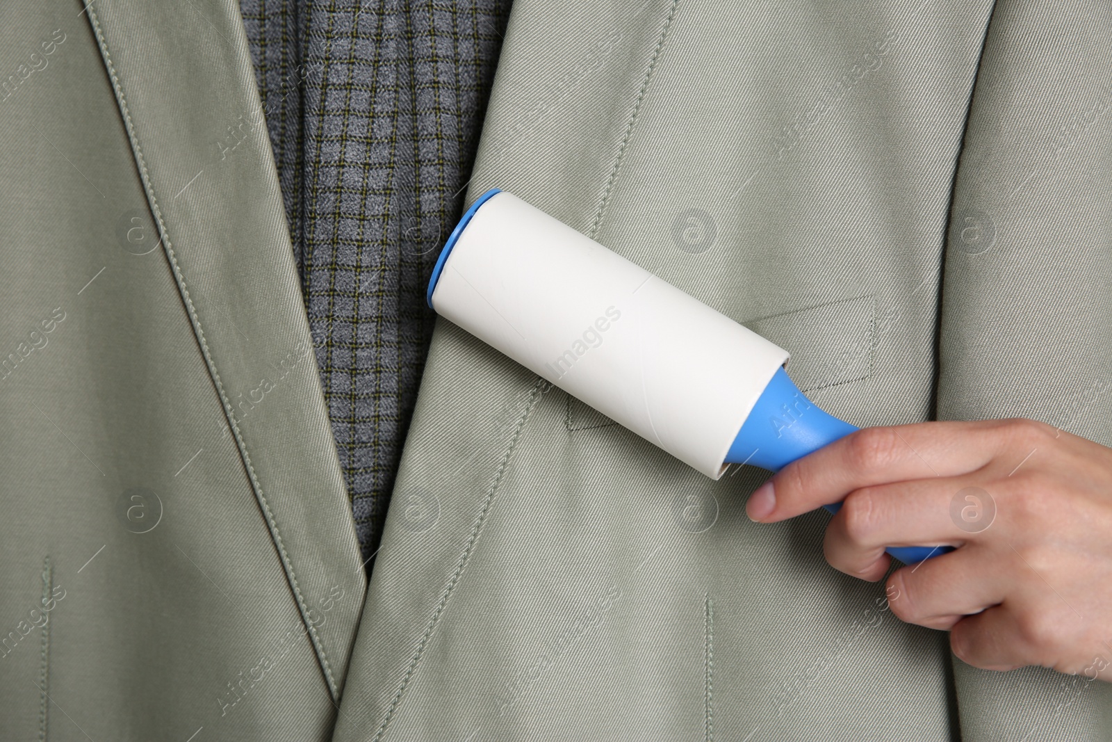 Photo of Woman cleaning light grey jacket with lint roller, closeup