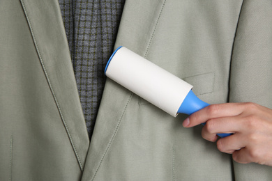 Photo of Woman cleaning light grey jacket with lint roller, closeup