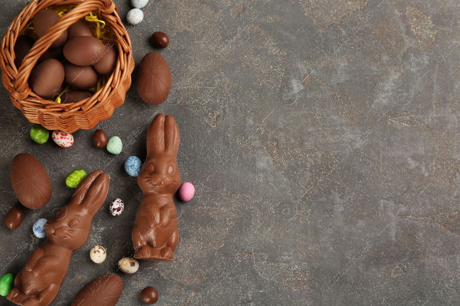 Photo of Flat lay composition with chocolate Easter bunnies, eggs and candies on grey table. Space for text