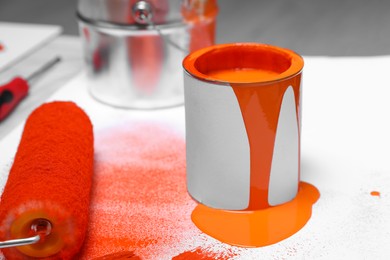 Photo of Cans of orange paint and roller on white table indoors