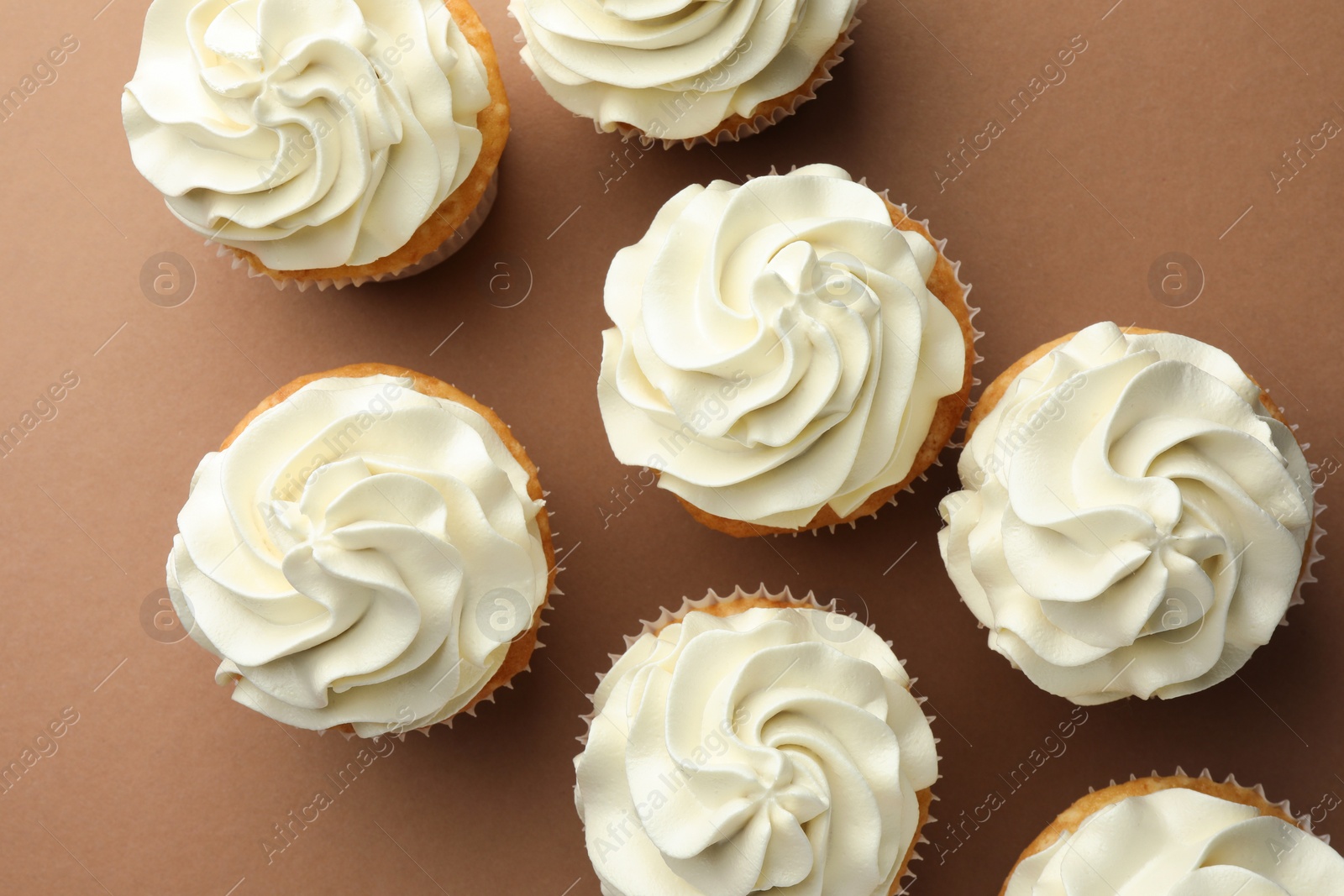 Photo of Tasty vanilla cupcakes with cream on dark beige background, top view