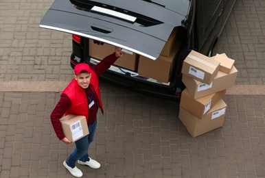 Courier with parcel near delivery van outdoors, above view