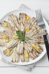 Photo of Tasty pickled anchovies with spices and fork on white wooden table, top view