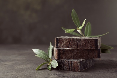 Photo of Handmade soap bars and olive leaves on grey table. Space for text