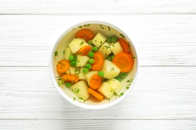 Bowl of fresh homemade vegetable soup on white wooden background, top view