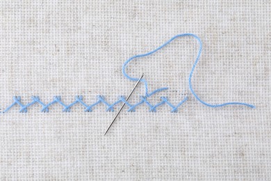 Embroidery stitches made with light blue thread and needle on canvas, top view