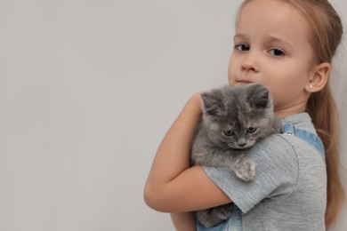 Photo of Cute little girl with kitten on light background, space for text. Childhood pet