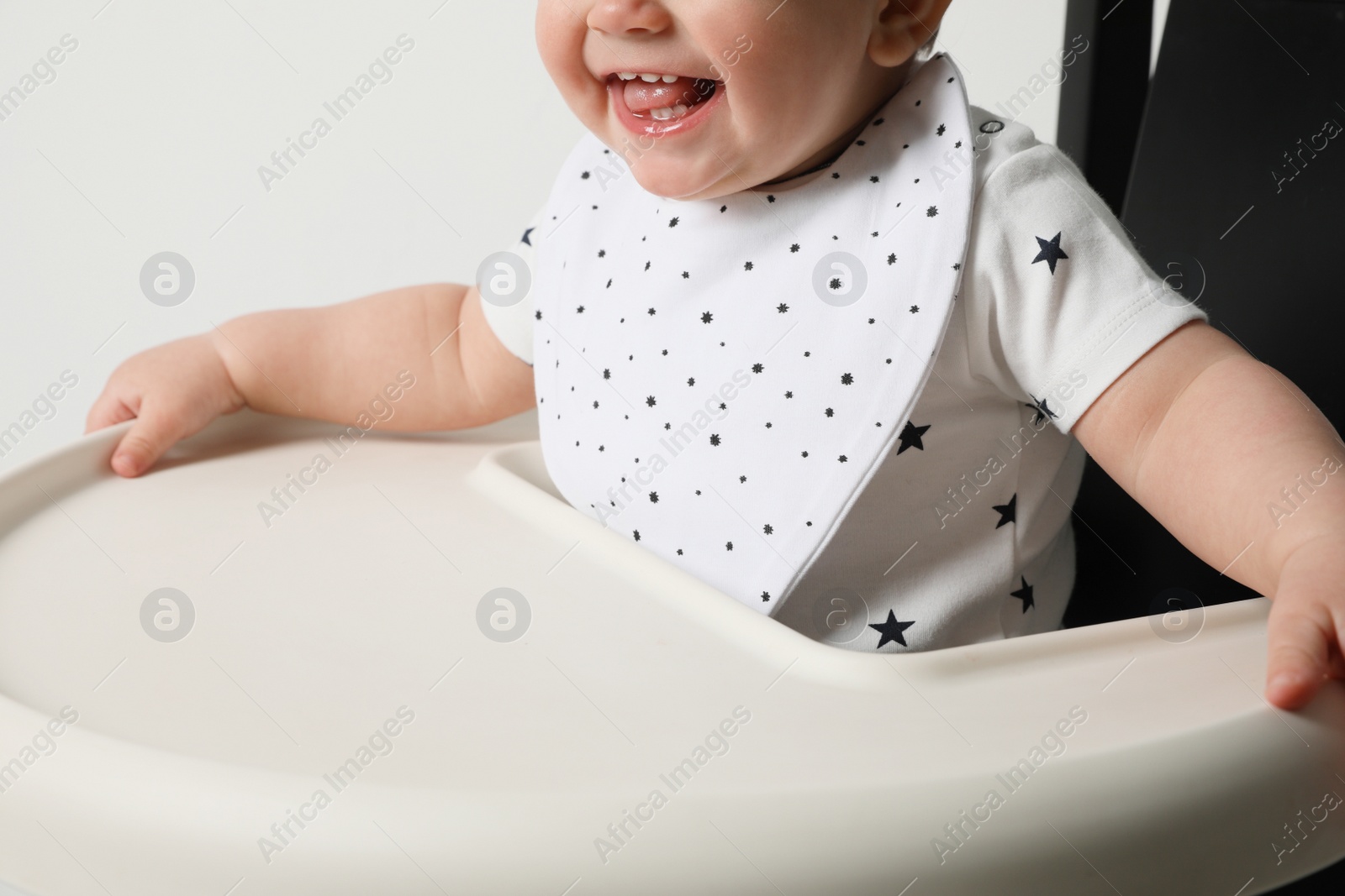 Photo of Cute little baby wearing bib in highchair on white background, closeup