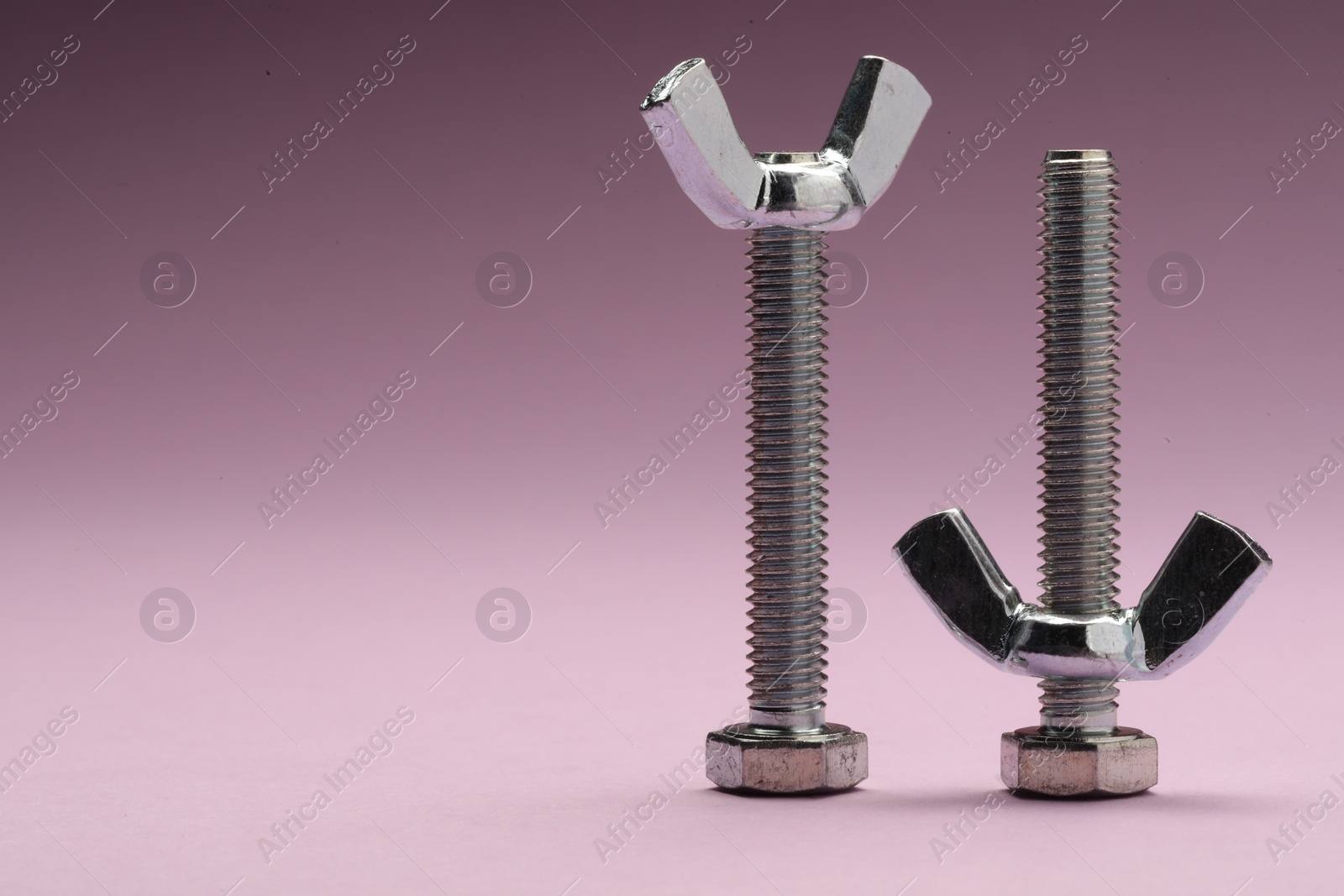 Photo of Metal screws with wing nuts on purple background, space for text
