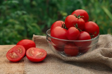 Photo of Bowl with cut and whole red tomatoes on wooden table in garden