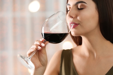 Photo of Beautiful young woman with glass of luxury red wine indoors, closeup view. Space for text