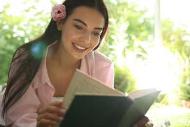 Beautiful young woman reading book in park on sunny day