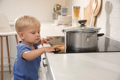 Photo of Curious little boy exploring electric stove in kitchen