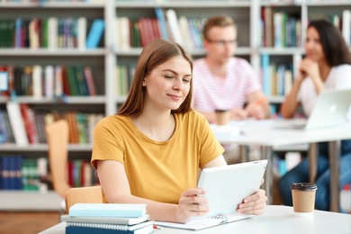 Photo of Young woman working on tablet at table in library