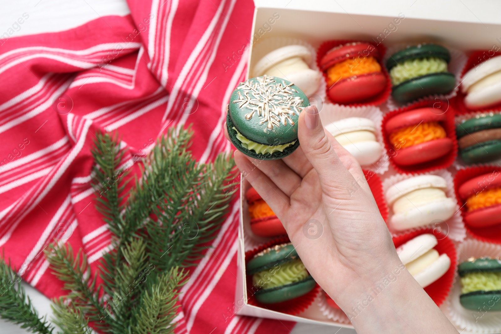 Photo of Woman with decorated Christmas macaron at table, closeup