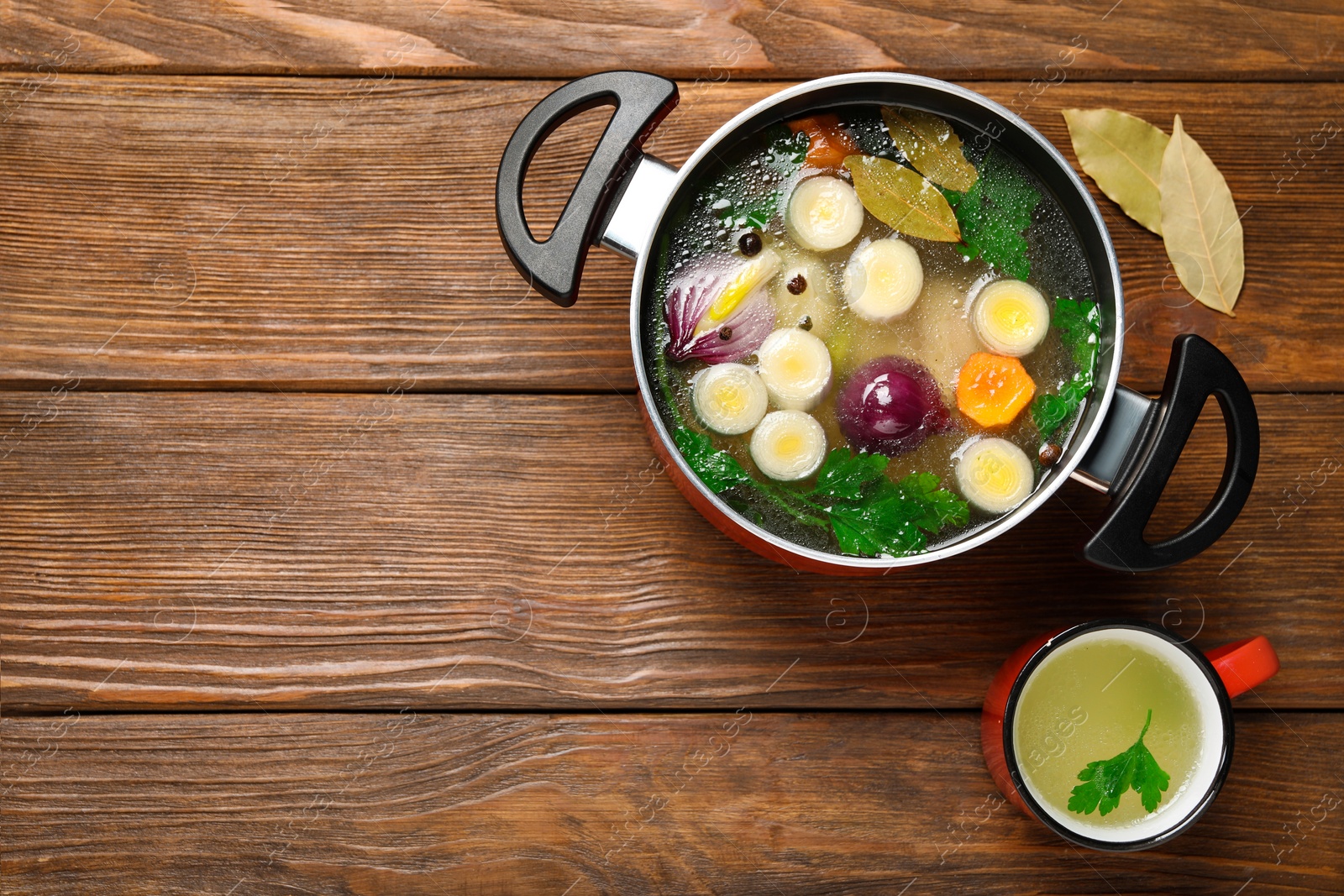 Photo of Tasty bouillon and bay leaves on wooden table, flat lay. Space for text