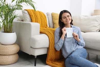 Photo of Young woman with greeting card on floor in living room