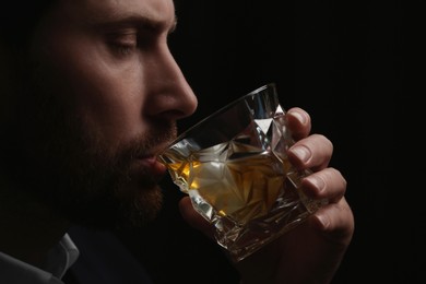 Photo of Man drinking whiskey on black background, closeup
