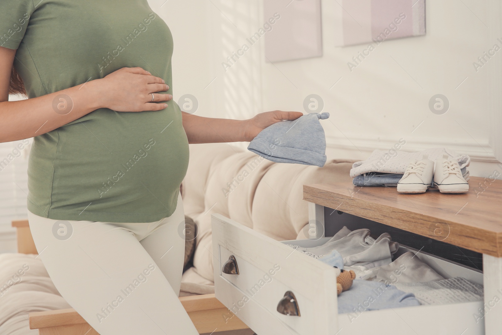 Photo of Pregnant woman holding baby hat at home, closeup