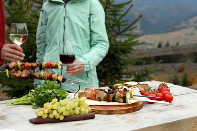 Photo of Friends having barbecue party outdoors, focus on table with delicious food