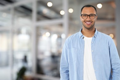 Handsome confident man with eyeglasses in office, space for text