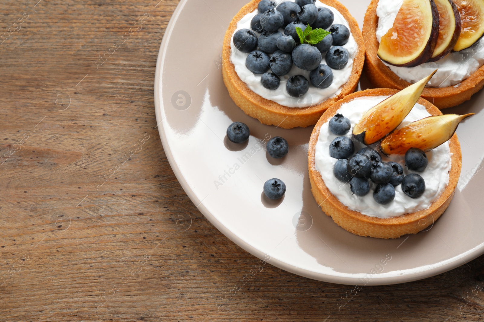 Photo of Tarts with blueberries and figs served on wooden table, top view with space for text. Delicious pastries