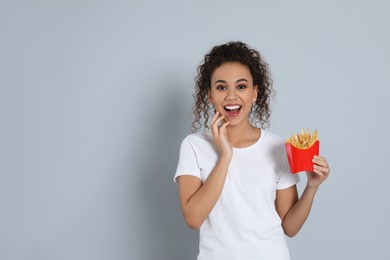 Photo of Excited African American woman with French fries on grey background, space for text