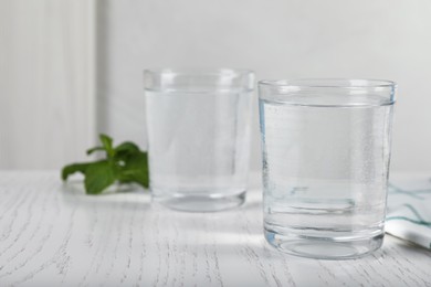 Photo of Glasses of soda water on white wooden table. Space for text