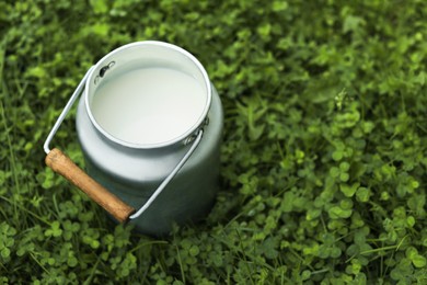 Photo of Can with fresh milk on green grass outdoors, space for text