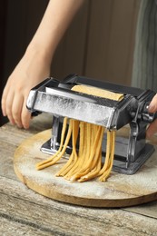 Photo of Woman making homemade noodles with pasta maker at wooden table, closeup