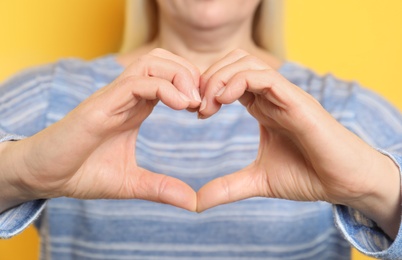 Photo of Mature woman making heart with her hands on color background, closeup view