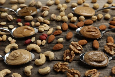 Photo of Tasty nut butters in spoons and raw nuts on wooden table, closeup