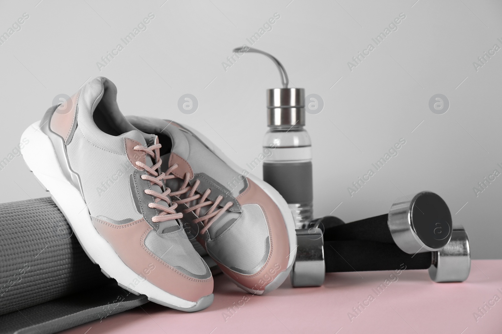 Photo of Composition of modern woman training shoes with mat, bottle and dumbbells on table