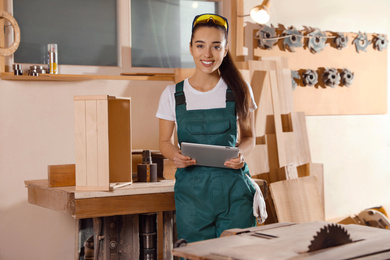 Photo of Professional carpenter in uniform with tablet near workbench
