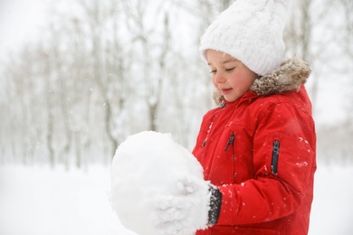Photo of Cute little girl holding snowball outdoors on winter day, space for text