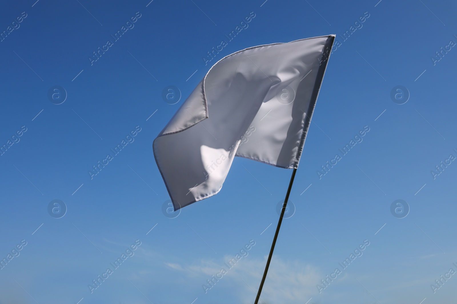 Photo of White flag fluttering against blue sky on sunny day