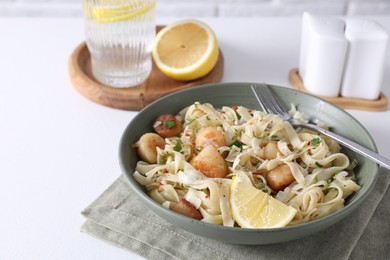 Delicious scallop pasta with spices and lemon in bowl served on white table, closeup