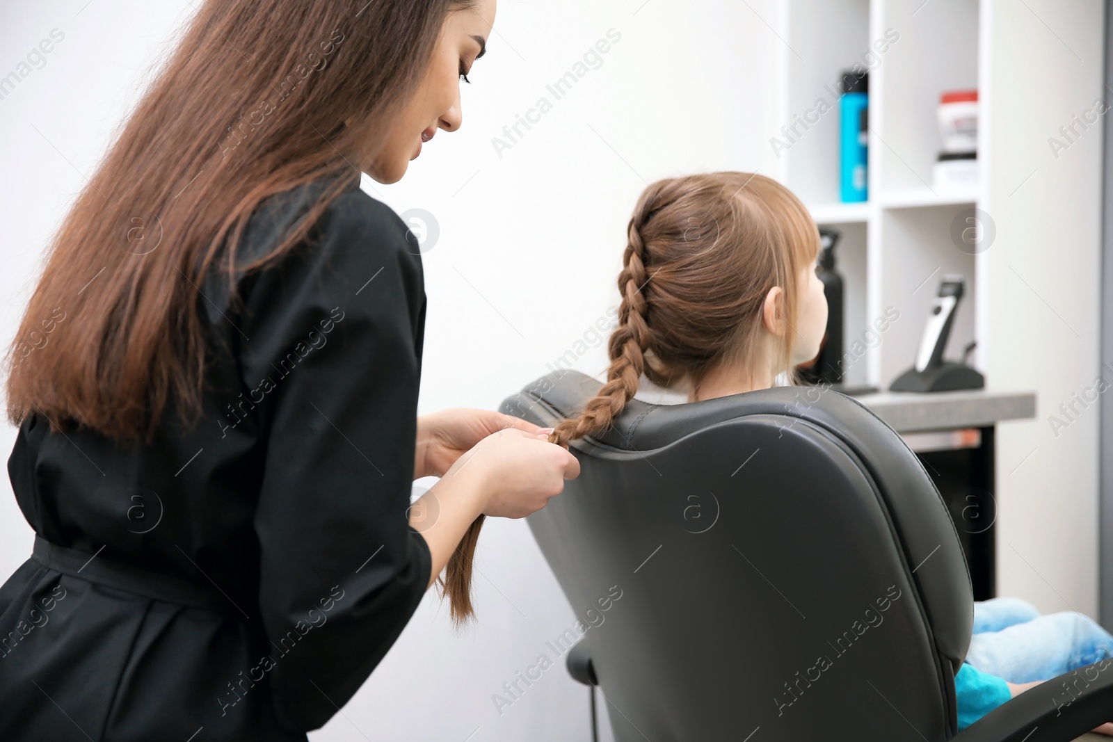 Photo of Professional female hairdresser working with little girl in salon