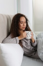 Photo of Beautiful African American woman with cup of drink in bed at home