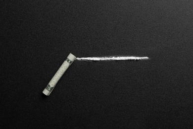 Photo of Line of cocaine and rolled money bill on dark background, top view