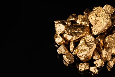 Photo of Pile of shiny gold nuggets on black background. Space for text