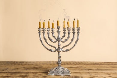 Photo of Silver menorah with candles on wooden table against beige background. Hanukkah celebration