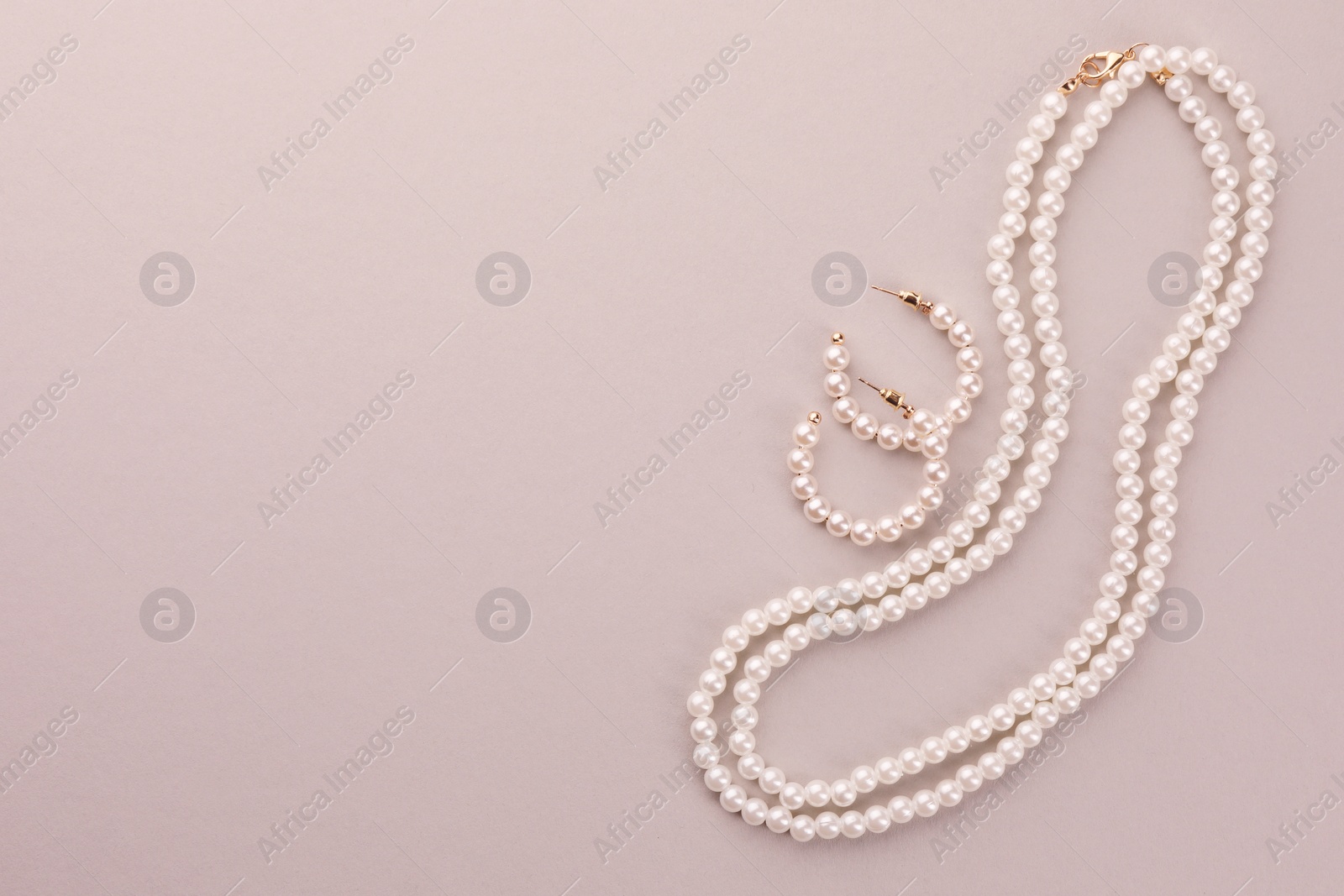 Photo of Elegant pearl necklace and earrings on beige background, top view. Space for text