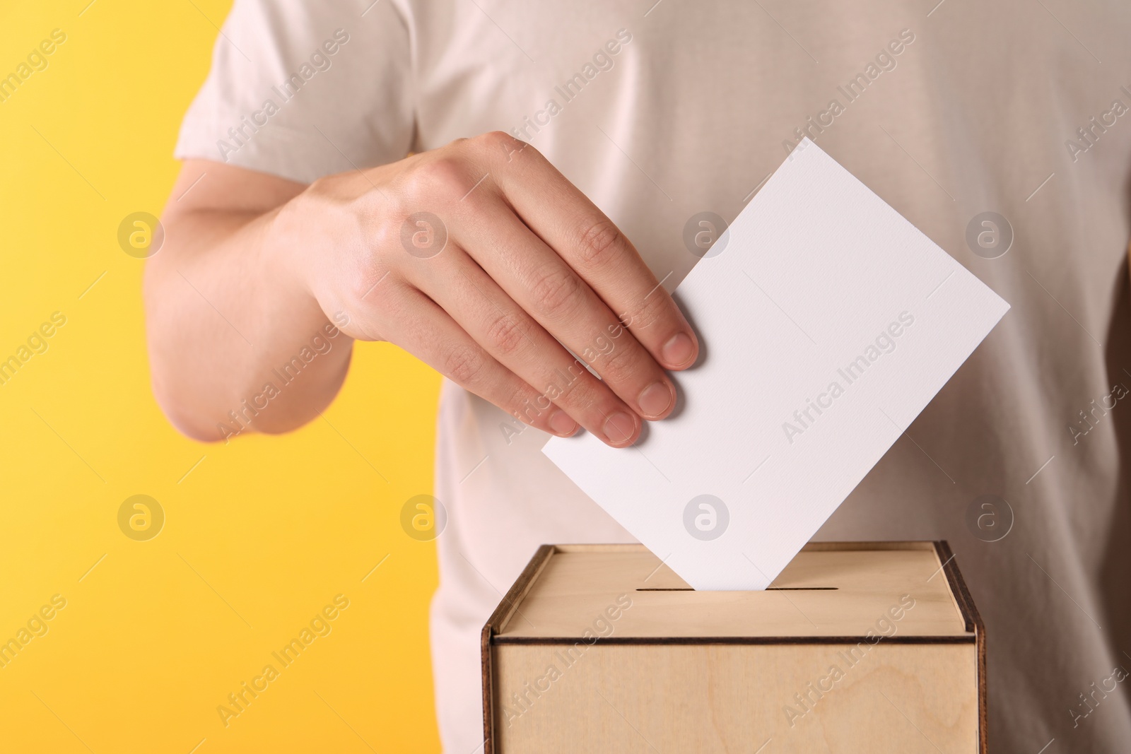 Photo of Man putting his vote into ballot box on yellow background, closeup