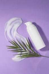 Photo of Bottle with cleansing foam and green leaves on violet background, flat lay. Cosmetic product