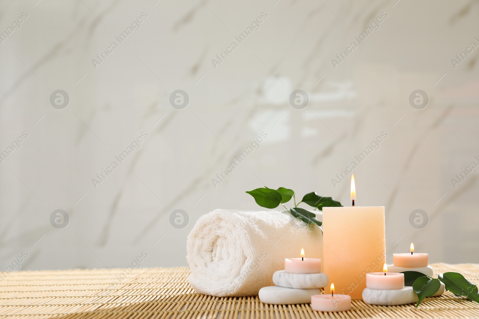 Photo of Composition of spa stones, towel and burning candles on bamboo mat, space for text