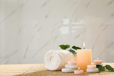 Composition of spa stones, towel and burning candles on bamboo mat, space for text