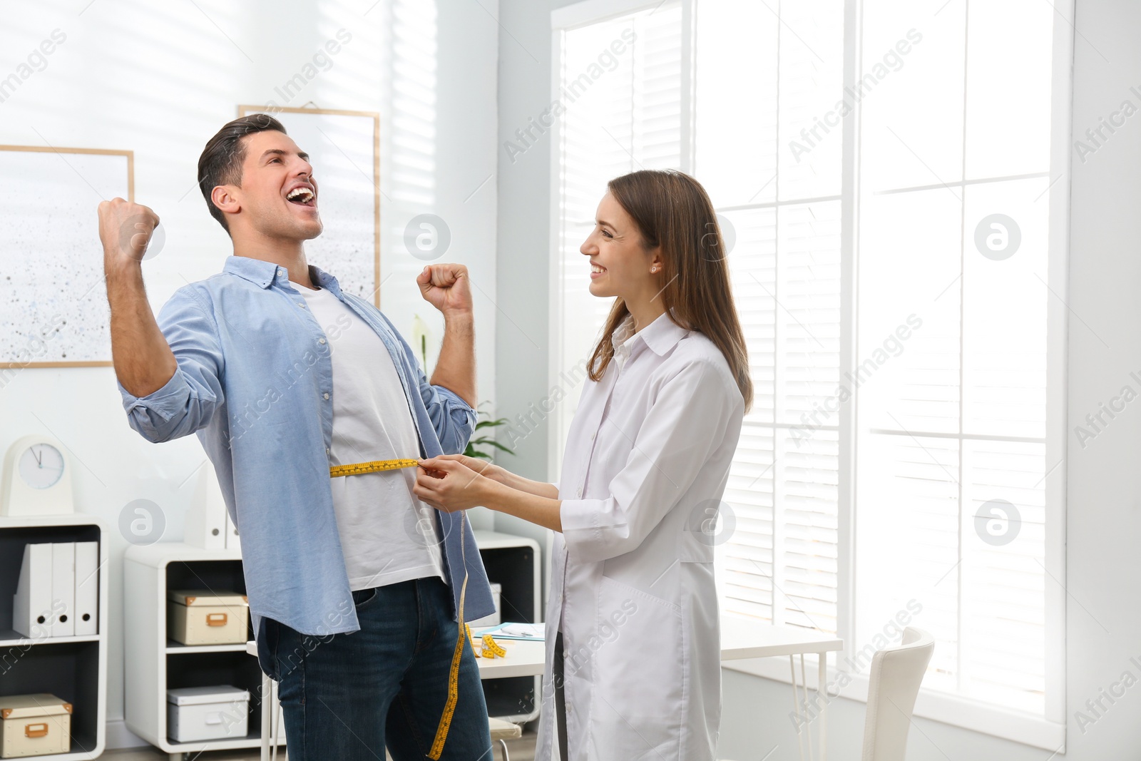 Photo of Young nutritionist measuring patient's waist in clinic