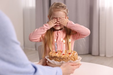 Photo of Birthday celebration. Mother holding tasty cake with burning candles near her daughter indoors