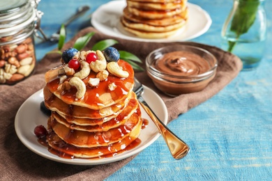 Stack of tasty pancakes with berries, nuts and syrup on table